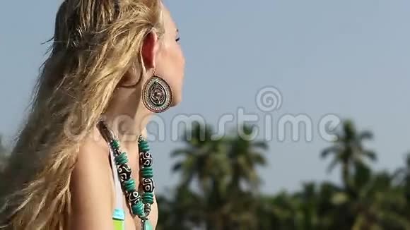 穿着泳装项链和耳环的特写金发女孩看着棕榈树视频的预览图