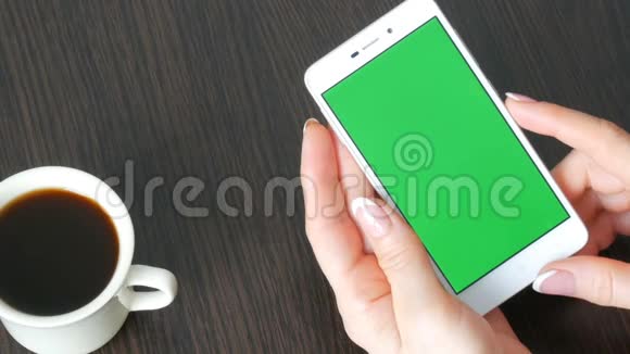 漂亮的法国美甲女性手拿着一个白色智能手机绿色屏幕靠近白色咖啡杯使用视频的预览图