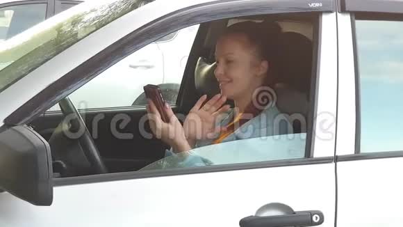 夏日夕阳西下一位红发的年轻美女坐在汽车车轮后面手里拿着手机视频的预览图