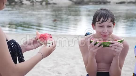 孩子们青少年在海滩上休息笑着吃西瓜慢动作视频男孩和生活方式女孩视频的预览图