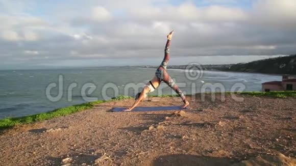 年轻女子在黎明或日落时在岩石上靠近海洋练习瑜伽视频的预览图