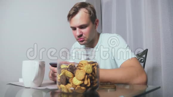 饥饿悲伤的男人晚上坐在客厅的一张桌子上他吃肝脏用她的智能手机视频的预览图