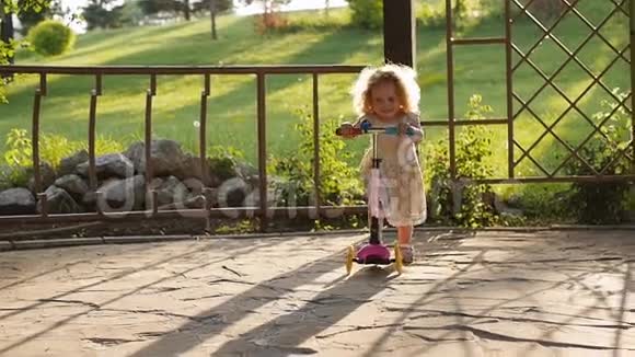 夏天公园里可爱的卷发小女孩骑摩托车视频的预览图