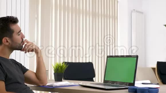 客厅里的男人看着电脑上的绿色模拟屏幕视频的预览图