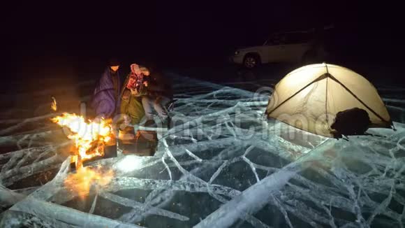 晚上有四个旅行者乘火在冰上在冰上露营帐篷就在火旁边周围的人都在变暖视频的预览图