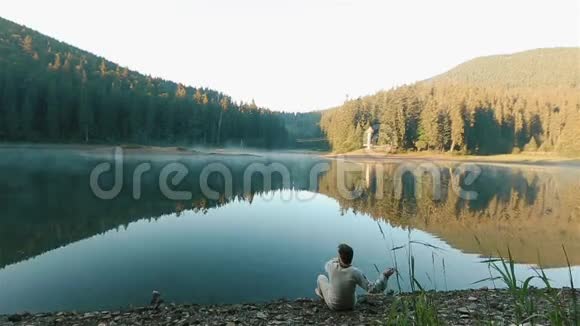 一个英俊体贴的年轻人穿着刺绣衬衫把石头扔进水里看着风景如画的山视频的预览图
