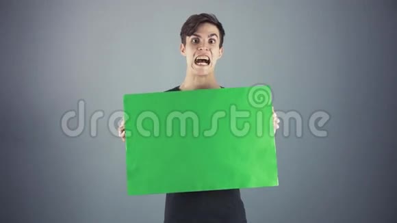 穿着黑色衬衫拿着绿色钥匙片海报灰色背景的年轻人视频的预览图