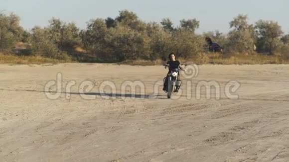 美丽的年轻女子骑着一辆古老的咖啡馆赛车摩托车在沙漠日落或日出女司机慢动作视频的预览图
