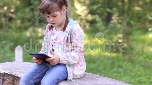 女孩坐在石墙上在公园玩平板电脑视频的预览图