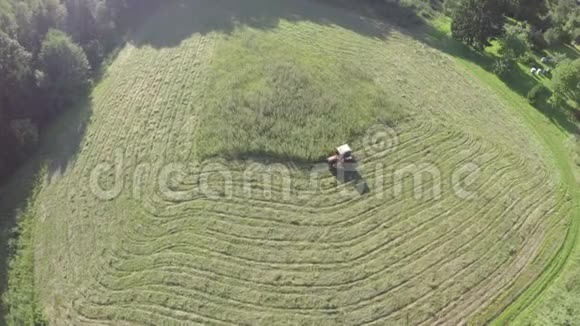 从农田的草地上割草的红色小老拖拉机鸟瞰视频的预览图