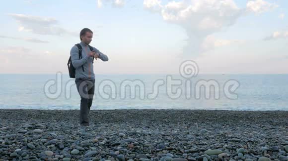 一个人沿着海滩散步检查海洋附近智能手表上的信息他对社会负责视频的预览图