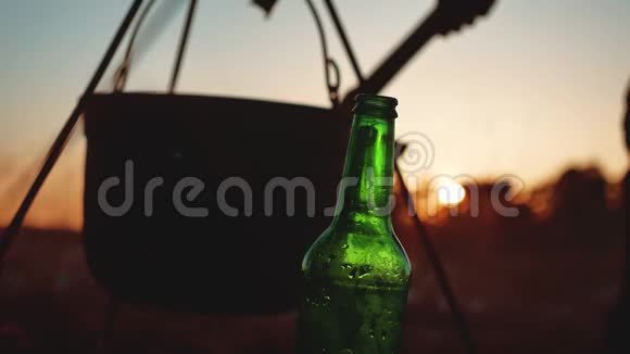 点燃一个大锅篝火一瓶啤酒在日落剪影露营特写旅游户外休闲生活方式视频的预览图