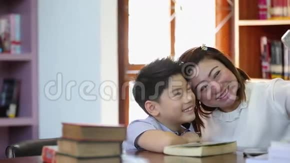 快乐的亚洲男孩和妈妈在图书馆用手机拍照视频的预览图
