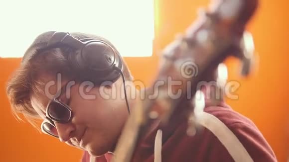 一个戴着耳机和眼镜的音乐家在录音室里弹吉他和录音视频的预览图