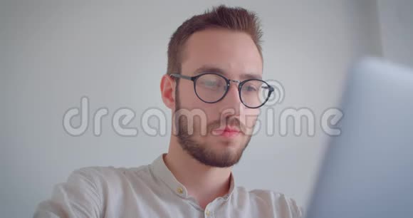 年轻英俊的白种人商人戴着眼镜在笔记本电脑上打字看着照相机的特写照片视频的预览图