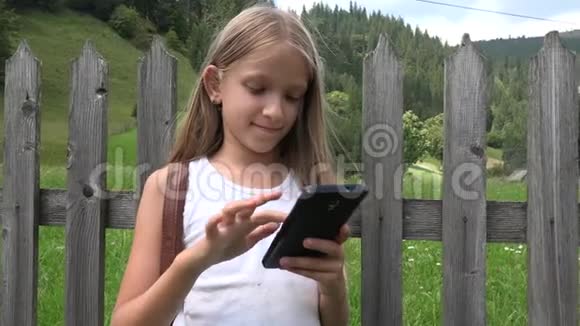 户外儿童玩智能手机桌上儿童大自然中的女孩放松视频的预览图