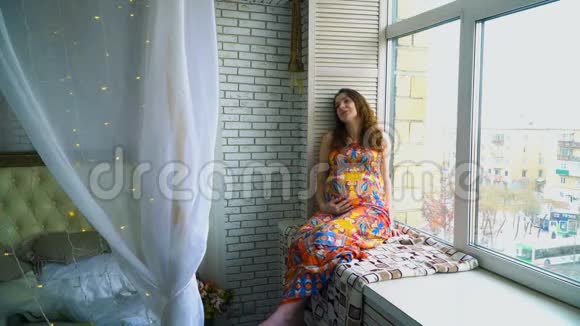 年轻漂亮的怀孕少女坐在窗边视频的预览图