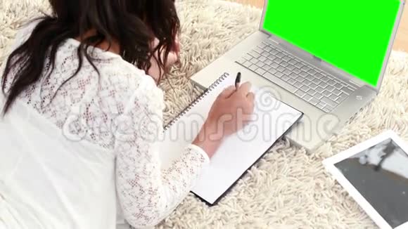 微笑的女人躺在地板上用笔记本做作业视频的预览图