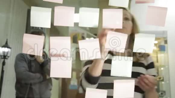 创意女商人和男人在现代玻璃办公室的头脑风暴会议使用不同颜色的贴纸视频的预览图