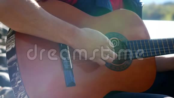 在阳光明媚的日子里盖伊在坐在河边的一把吉他上缓慢地演奏3840x21604k视频的预览图