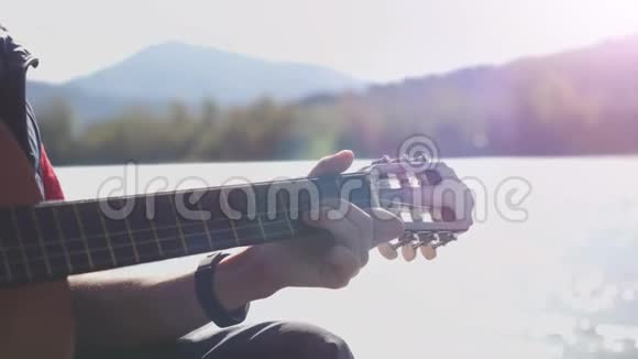 在阳光明媚的日子里盖伊在坐在河边的一把吉他上缓慢地演奏3840x2160视频的预览图