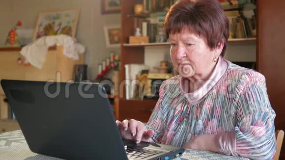 一位年长的妇女在家里用笔记本电脑检查社交网络上的信息她坐在桌边视频的预览图