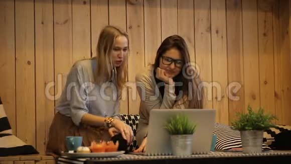 两个女孩坐在咖啡馆里看着笔记本电脑视频的预览图