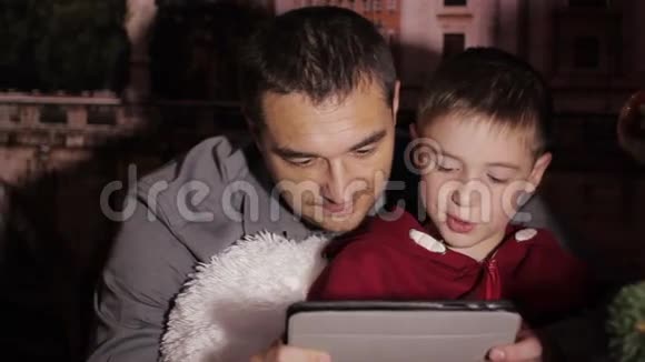 父亲和儿子在圣诞树上玩平板电脑视频的预览图