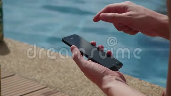 使用智能手机坐在室外别墅的泳池旁的贴身商人3840x2160视频的预览图