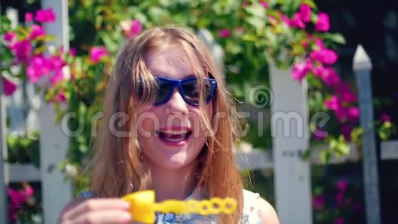 快乐的微笑少女白种人的外表微笑的看着相机在夏天的户外吹肥皂泡视频的预览图