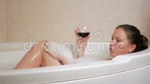 漂亮的女孩用一杯酒泡澡一个大大的白色澡盆脸上洋溢着喜悦松弛概念视频的预览图