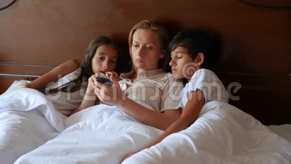 一个幸福的家庭躺在床上看着他们的智能手机上的东西4K慢动作视频的预览图
