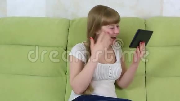 年轻女孩坐在沙发上在平板电脑上用Skype聊天她的男朋友坐下来继续参加视频的预览图