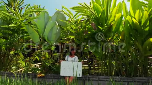 年轻女子手持白板带文字旅行旅行概念飞行无人机镜头绿色背景巴厘岛视频的预览图