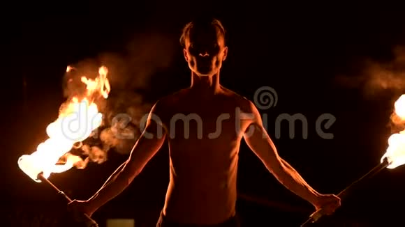 特写镜头低调年轻的男性长着长发赤裸的躯干在黑色的夜晚缓慢地旋转燃烧的火炬视频的预览图