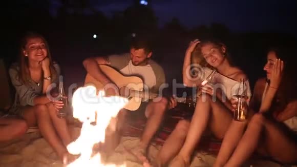 日落海滩派对篝火晚会朋友们围坐在篝火旁喝着啤酒对着吉他唱歌男子和男子视频的预览图
