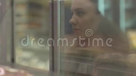站在冰箱里放肉的货架旁边的年轻女子视频的预览图