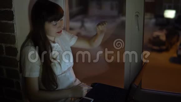 一位商务女性坐在靠近一扇黑窗的窗台上在笔记本电脑上工作视频的预览图