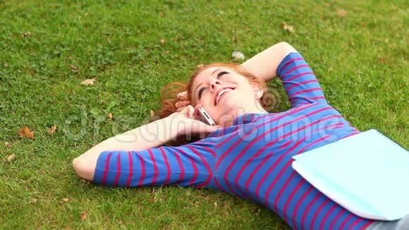 微笑的学生躺在草地上打电话视频的预览图