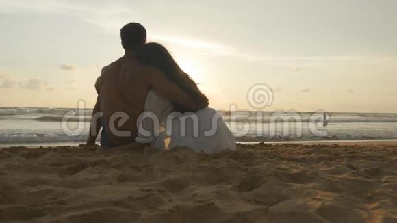 年轻的浪漫夫妇正在享受美丽的日落坐在海滩上拥抱一个女人和一个男人坐在一起视频的预览图