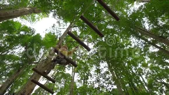 一个穿着安全装备的小男孩在森林探险公园的树梢上爬上了一条路线他爬上去视频的预览图