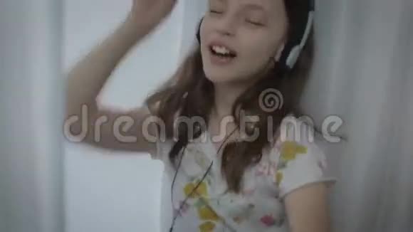 戴着耳机的漂亮小女孩有感情地唱着歌在窗口跳舞视频的预览图