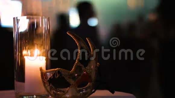 在一个俱乐部的桌子上人们在一个杯子里放着一支点燃的蜡烛和一个狂欢节面具的特写镜头视频的预览图