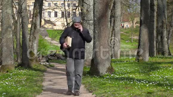 一个拿着两本书的人用智能手机说话在公园里散步视频的预览图