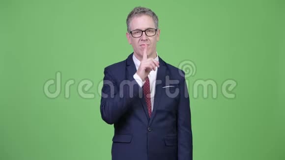 一张成熟商人用手指在嘴唇上拍摄的摄影棚视频的预览图