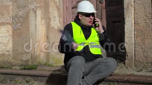 愤怒的建筑督察坐着用智能手机说话视频的预览图