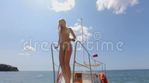 戴墨镜和比基尼的金发女郎在海滩上的游艇上摆姿势视频的预览图