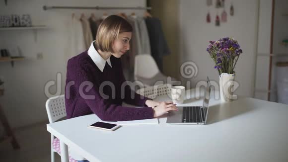 年轻女子坐在桌子旁在家里的键盘上打字视频的预览图