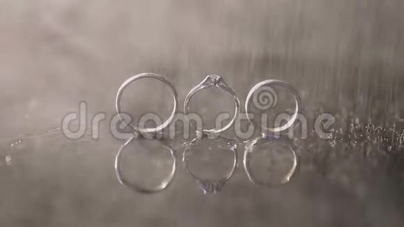 婚礼戒指和订婚戒指躺在黑暗的水面上用光线照亮宏观水溅了雨水视频的预览图