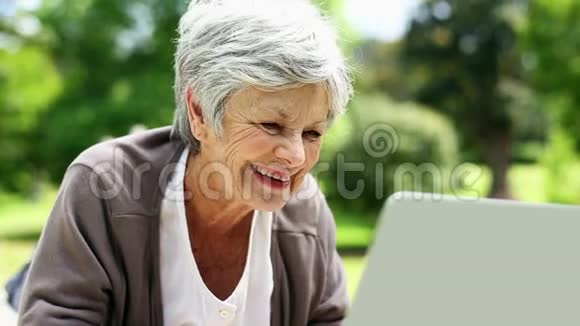 快乐的老年女性使用笔记本电脑在公园放松视频的预览图